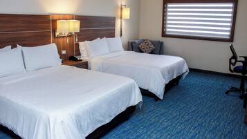 A hotel room with two beds, a nightstand with a lamp, a chair, and a window with blinds.