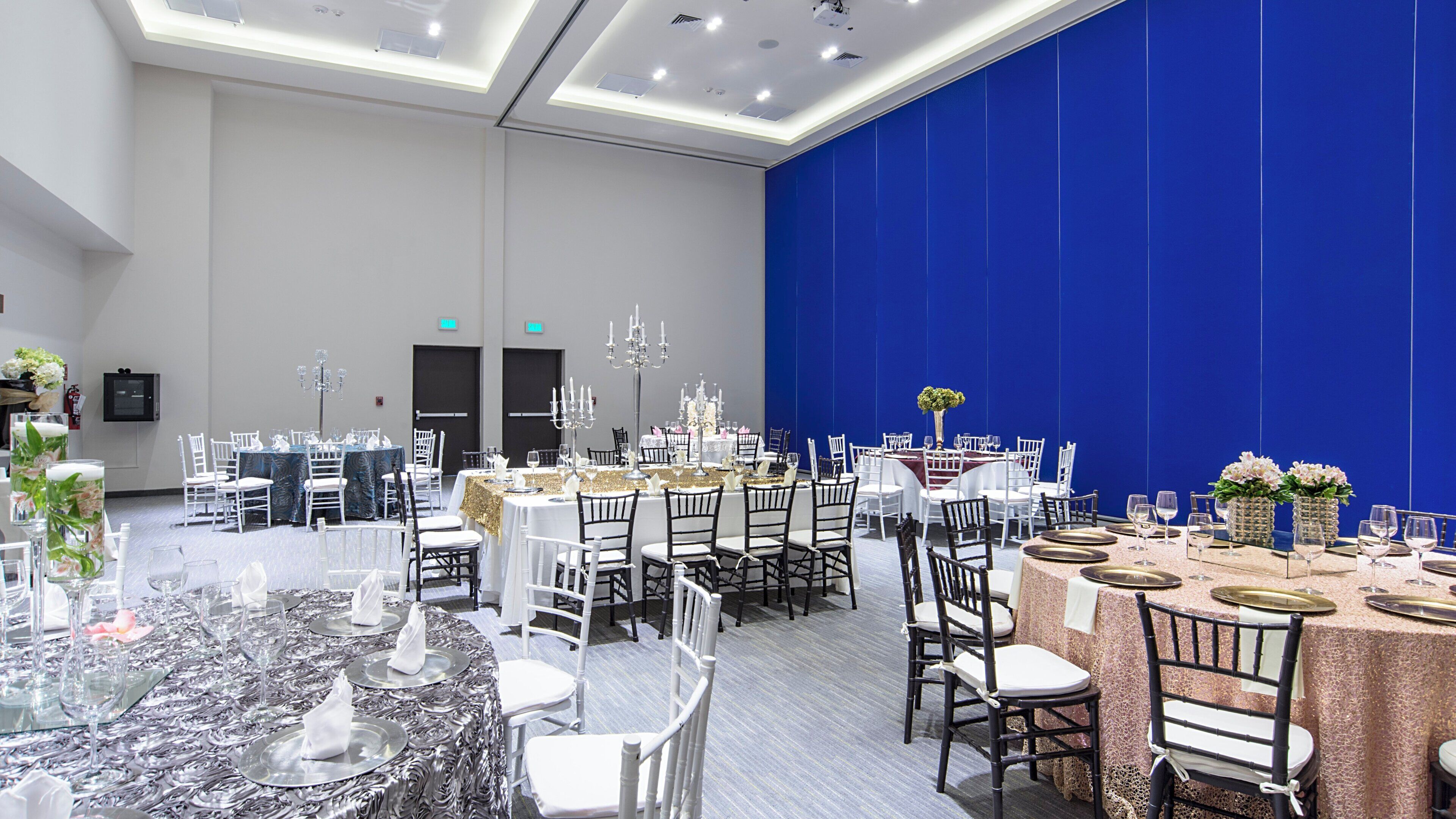 A banquet hall with round tables set for dining, white chairs, and chandeliers.