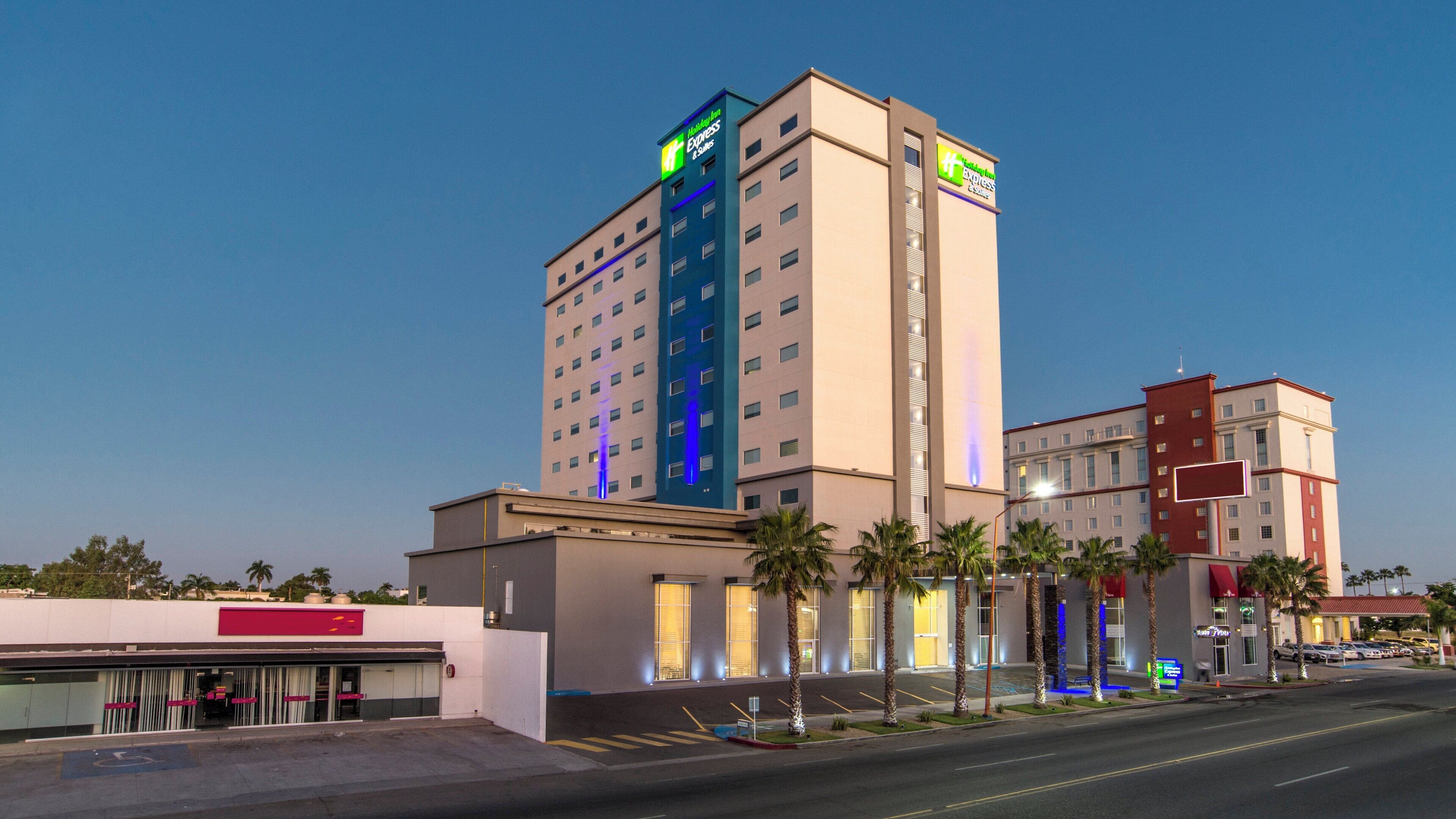 Ein mehrstöckiges Hotel mit auffälligem Holiday Inn Express Schild, einem Parkplatz und Palmen.