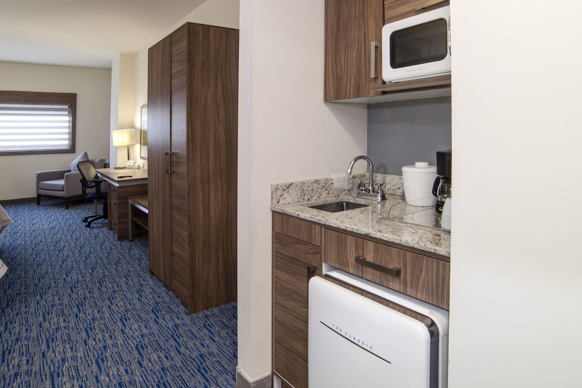 A hotel room with a bed, a desk, a chair, a microwave, a coffee maker, and a sink.