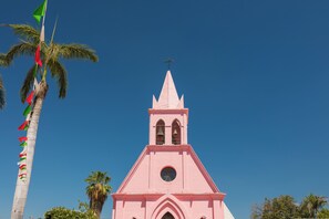 Une église rose avec un clocher, des palmiers et des drapeaux.