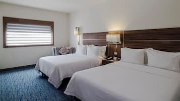 Habitación de hotel con dos camas, una mesita de noche con lámpara, una ventana con persianas y una alfombra azul.