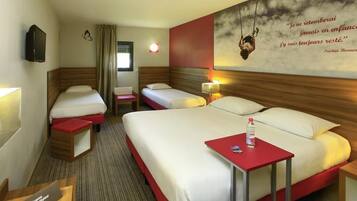 A hotel room with two beds, a red table, a TV, and a wall with a quote.