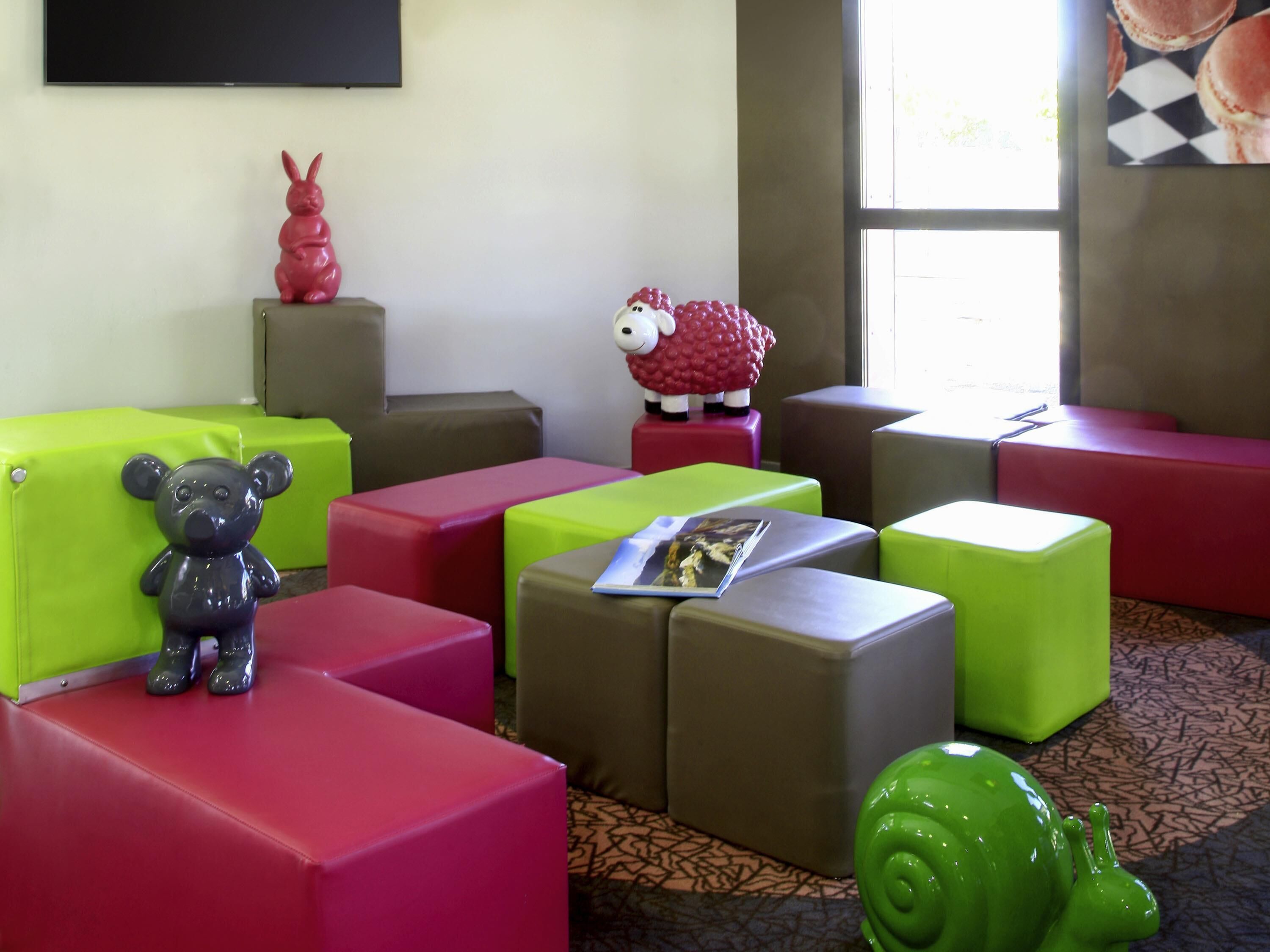A room with colorful seating arrangements, a bear figurine, a sheep figurine, and a magazine on a cushion.