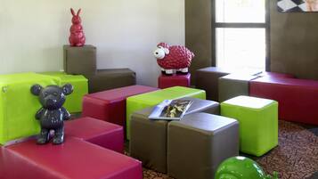 A room with colorful seating arrangements, a bear figurine, a sheep figurine, and a magazine on a cushion.