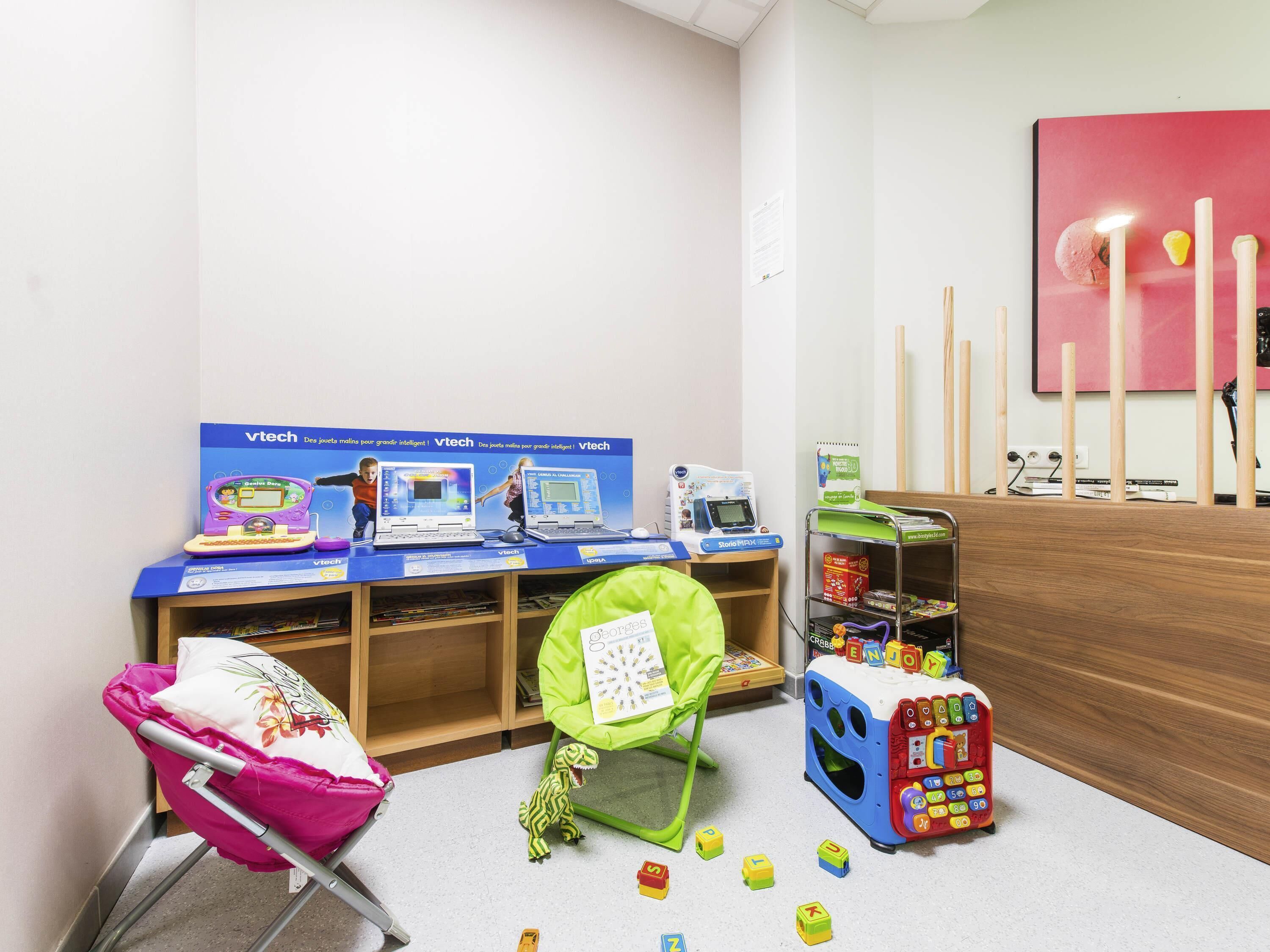 Zona de juegos infantiles con juguetes educativos, una computadora y una silla verde.
