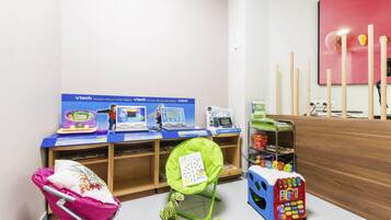 Zona de juegos infantiles con juguetes educativos, una computadora y una silla verde.