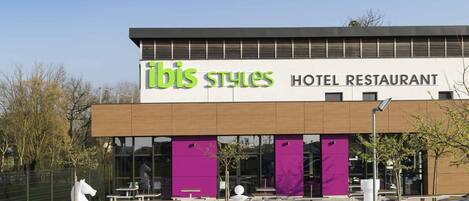 A modern hotel restaurant with a prominent sign, outdoor seating, and distinctive purple pillars.