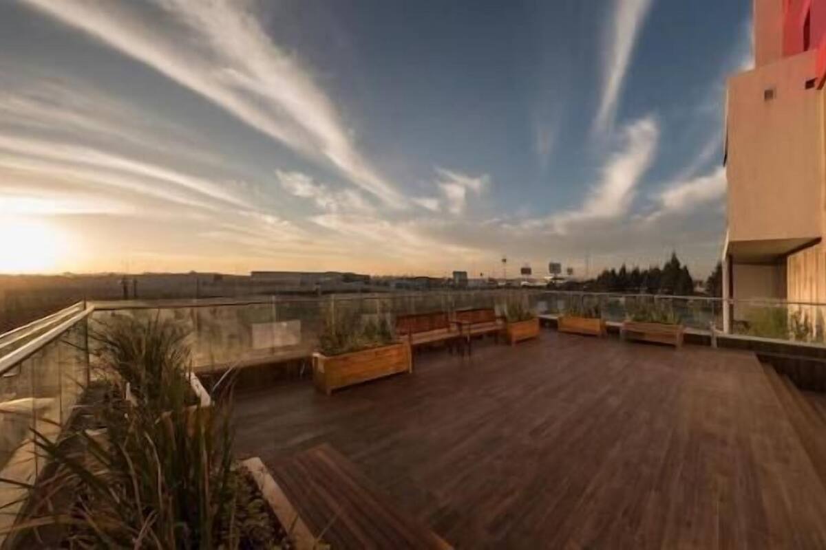 A rooftop terrace with wooden flooring, planters, and a glass railing.