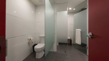 Un baño moderno con inodoro, mampara de vidrio y puerta roja.