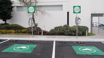 A parking area with electric vehicle charging stations, marked parking spaces, and a building in the background.