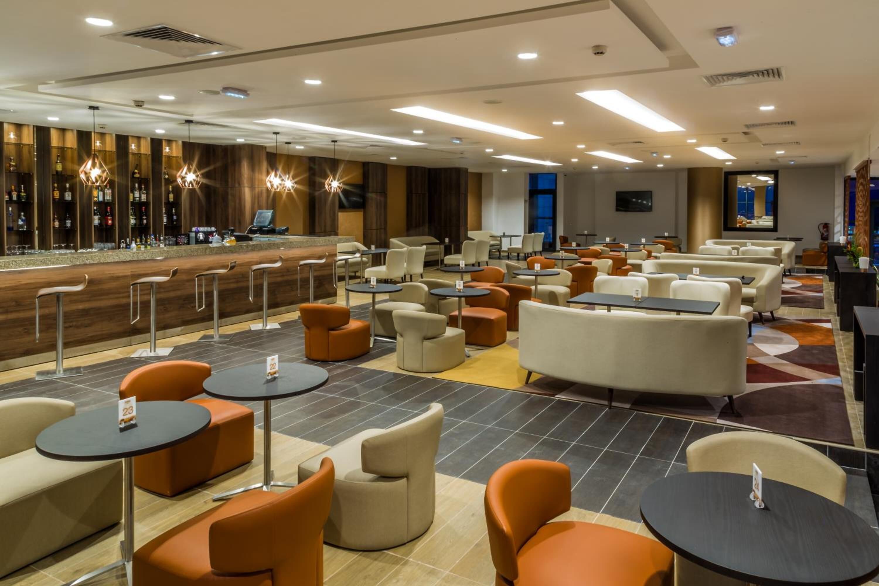 A hotel lobby with a bar area, multiple seating options including sofas and round tables, and a modern interior design.