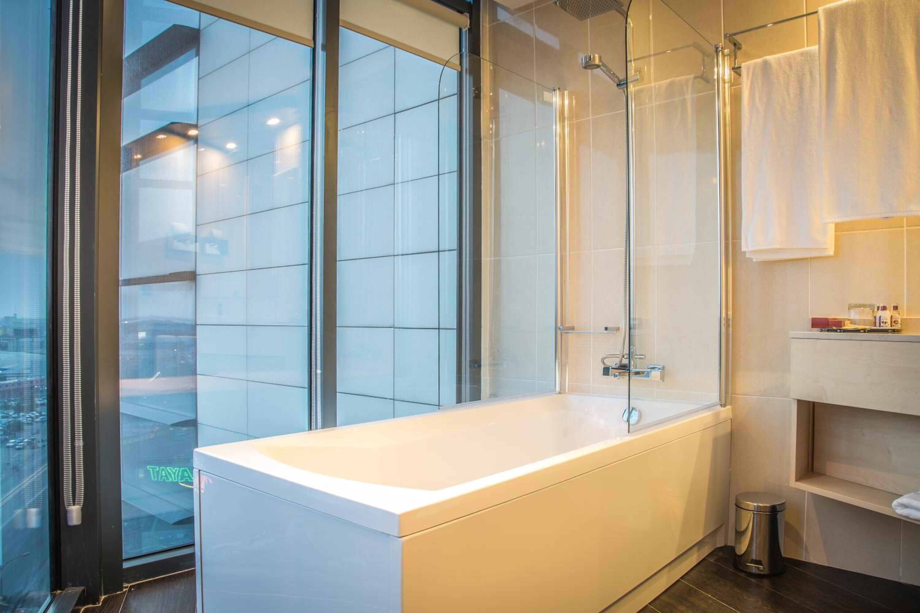 Ein modernes Badezimmer mit einer großzügigen Badewanne, einer Duschkabine aus Glas und Blick auf die Stadt durch bodentiefe Fenster.
