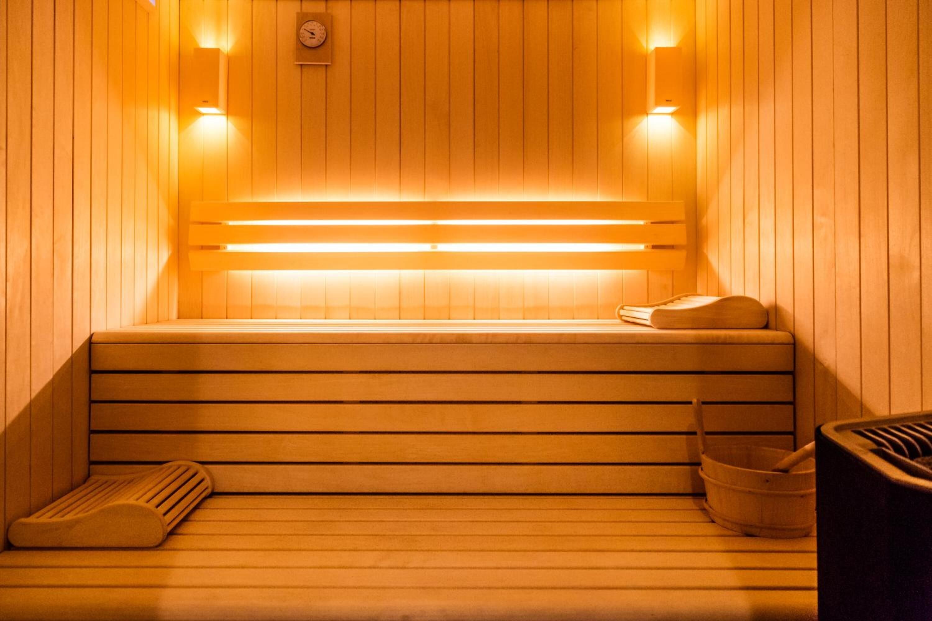 A sauna with wooden benches, a bench heater, and a wooden bucket.