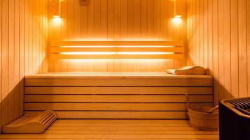 A sauna with wooden benches, a bench heater, and a wooden bucket.