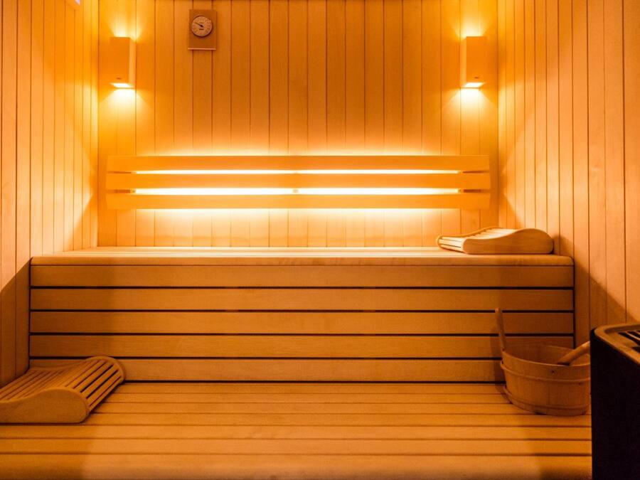 A sauna with wooden benches, a bench heater, and a wooden bucket.
