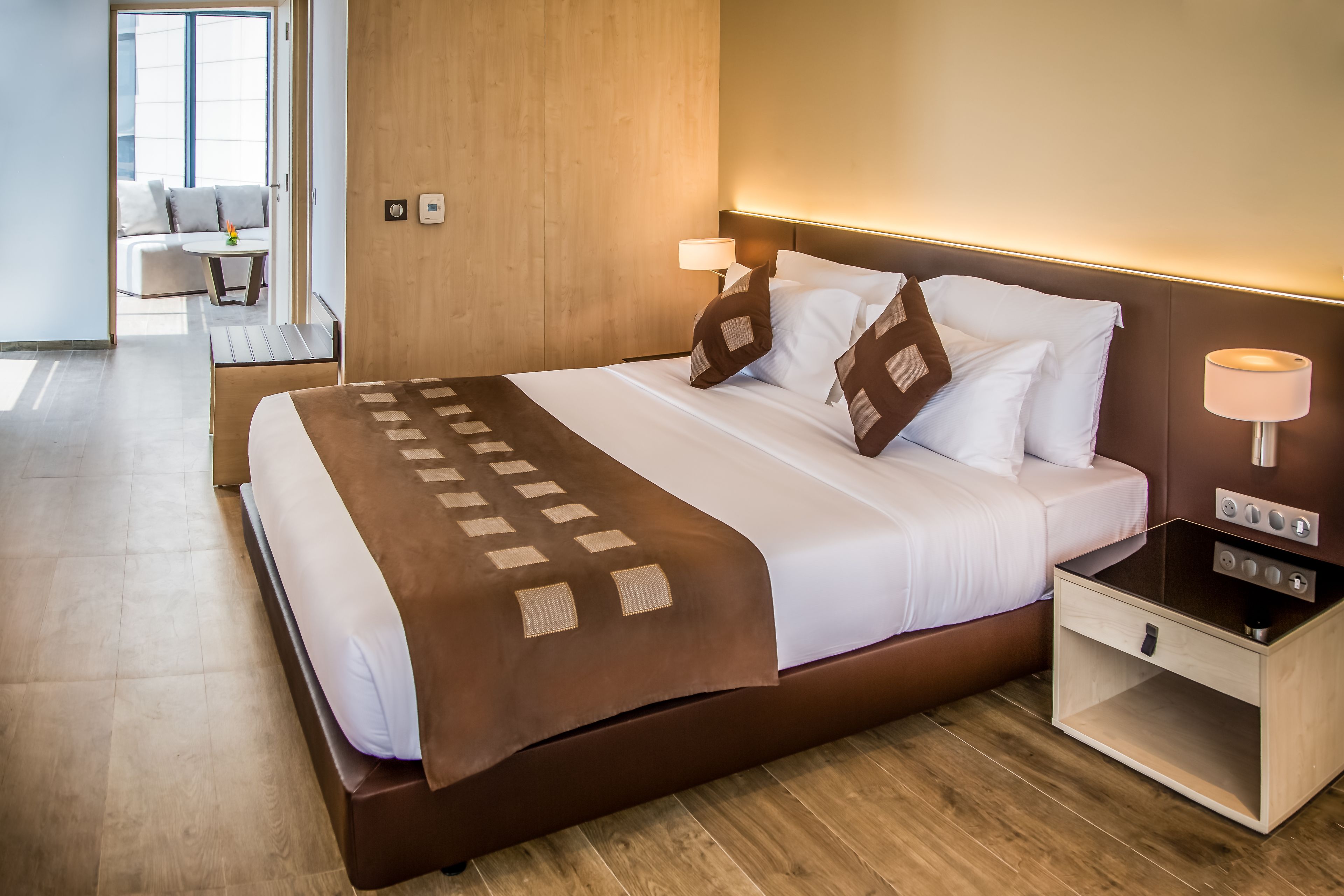 A modern hotel room with a large bed, bedside lamps, and a wooden headboard.