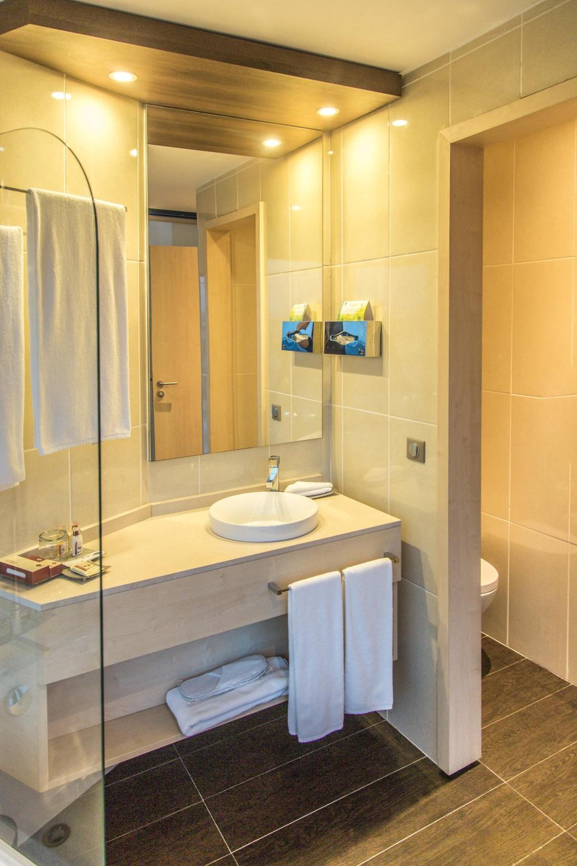 A modern bathroom with a glass shower enclosure, a round sink, and a large mirror.