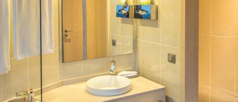 A modern bathroom with a glass shower enclosure, a round sink, and a large mirror.