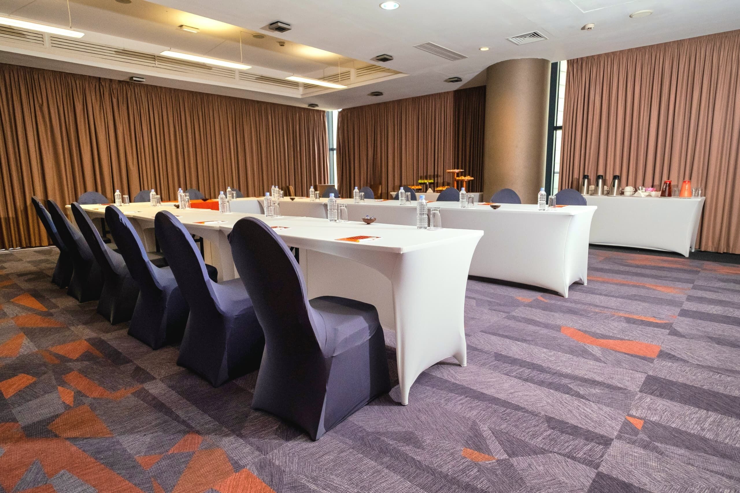 A conference room with long tables, chairs, and a carpeted floor.