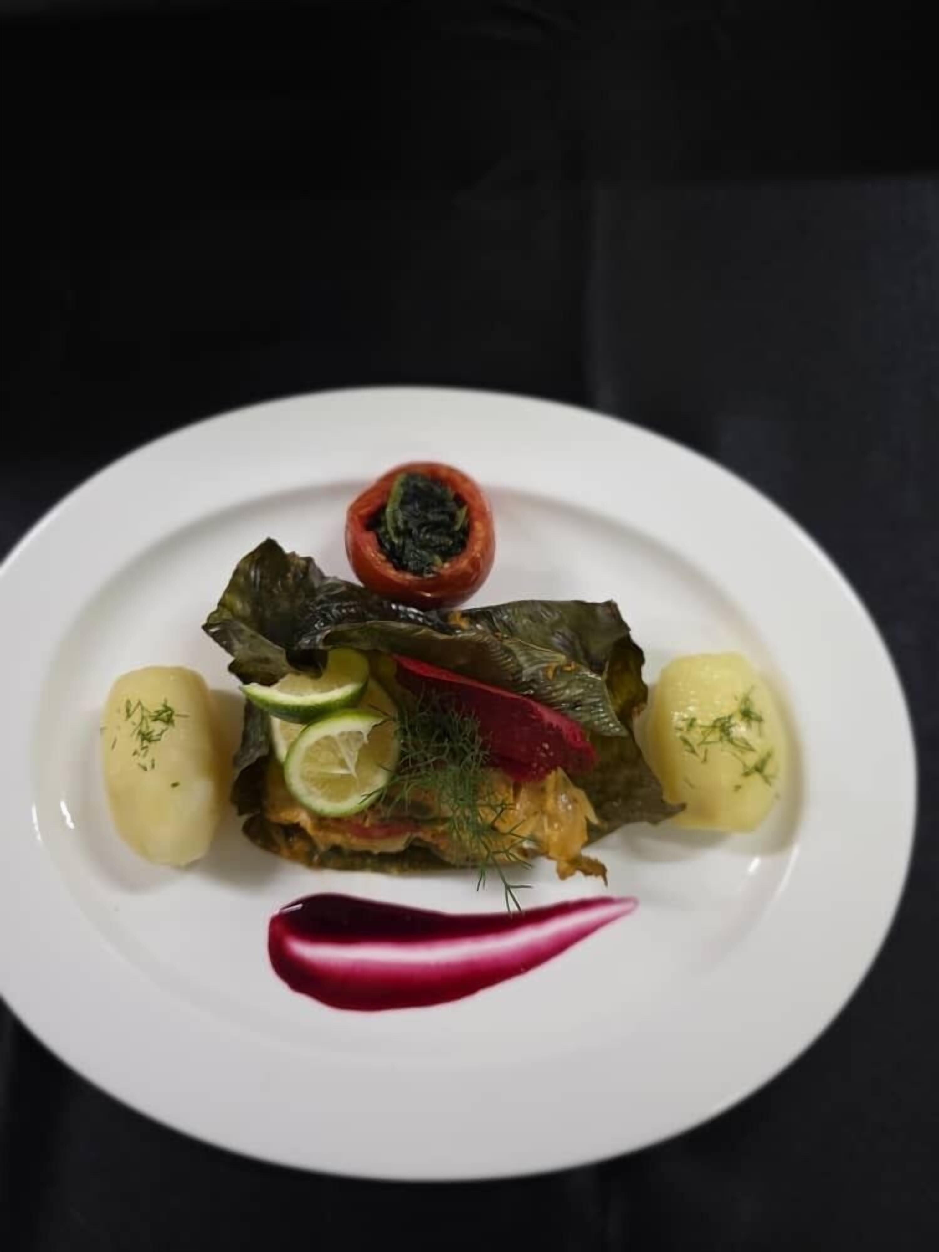 Une assiette de feuilles de vigne farcies, un poivron rouge et deux pommes de terre bouillies, le tout garni d’aneth.