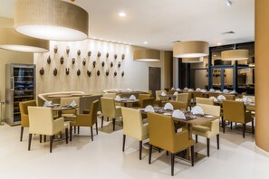A restaurant with multiple tables and chairs, a wall with decorative masks, and large hanging lamps. - Azalai Hôtel Abidjan (Abidjan)