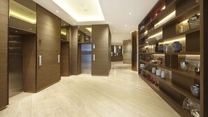 A modern hotel corridor with wooden paneling, a central elevator, and a display of decorative vases on shelves. - Ashley Wahid Hasyim Jakarta (Jakarta)