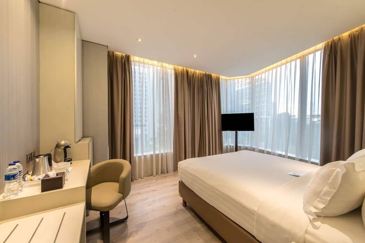 A hotel room with a bed, a desk with a chair, a TV, and a large window with curtains.
