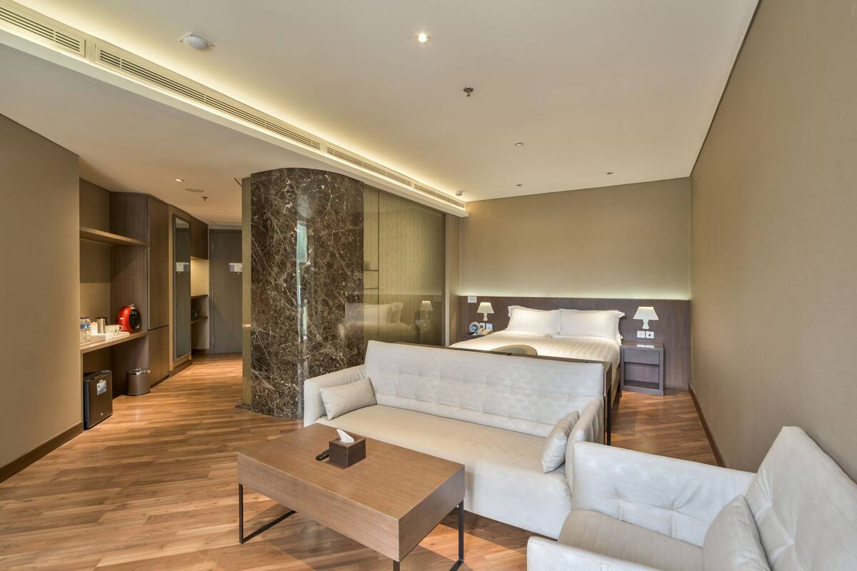 A modern hotel room with a large bed, a sofa, a desk, and a mirror.