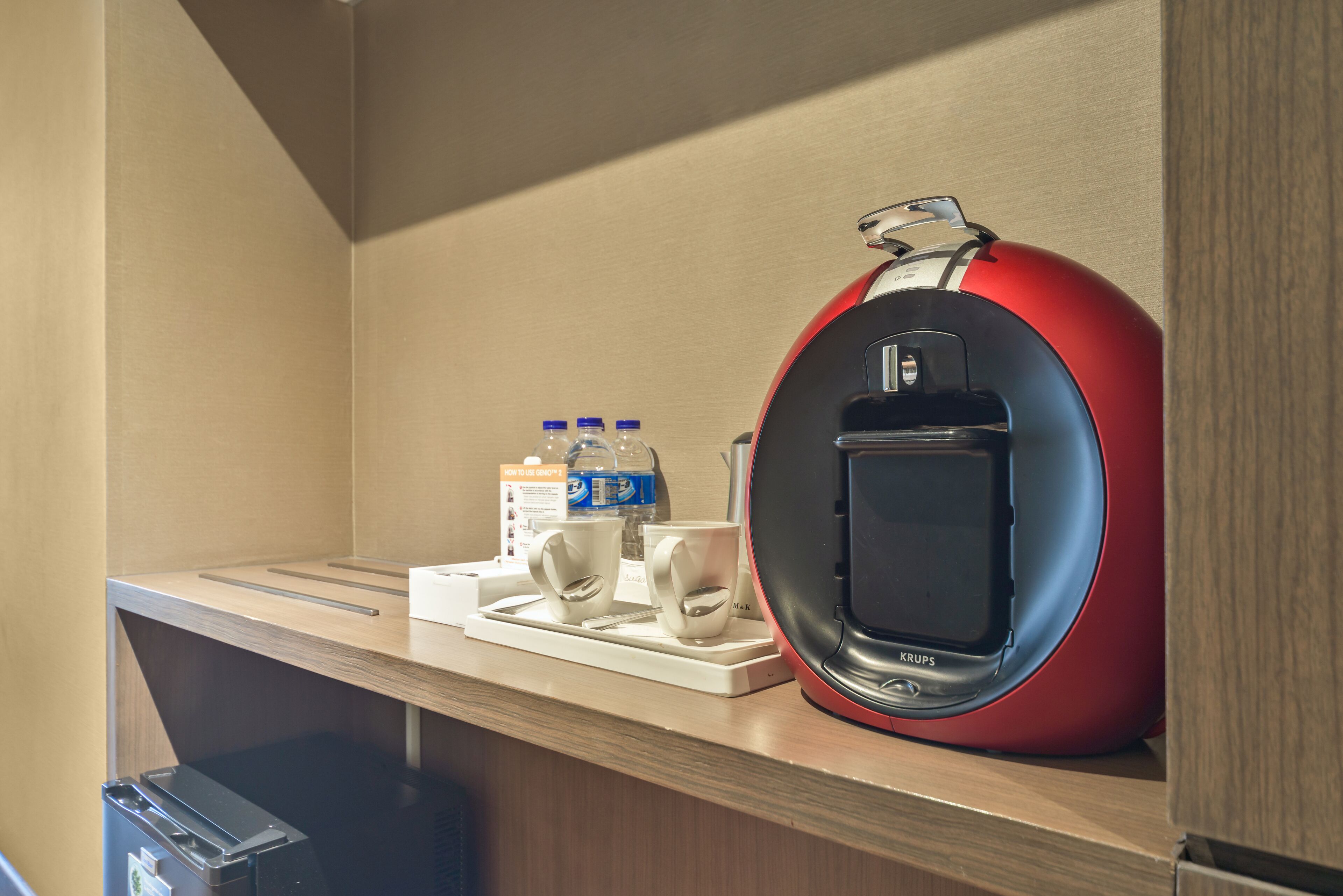 A compact kitchenette with a coffee maker, two cups, and bottled water on a wooden countertop.