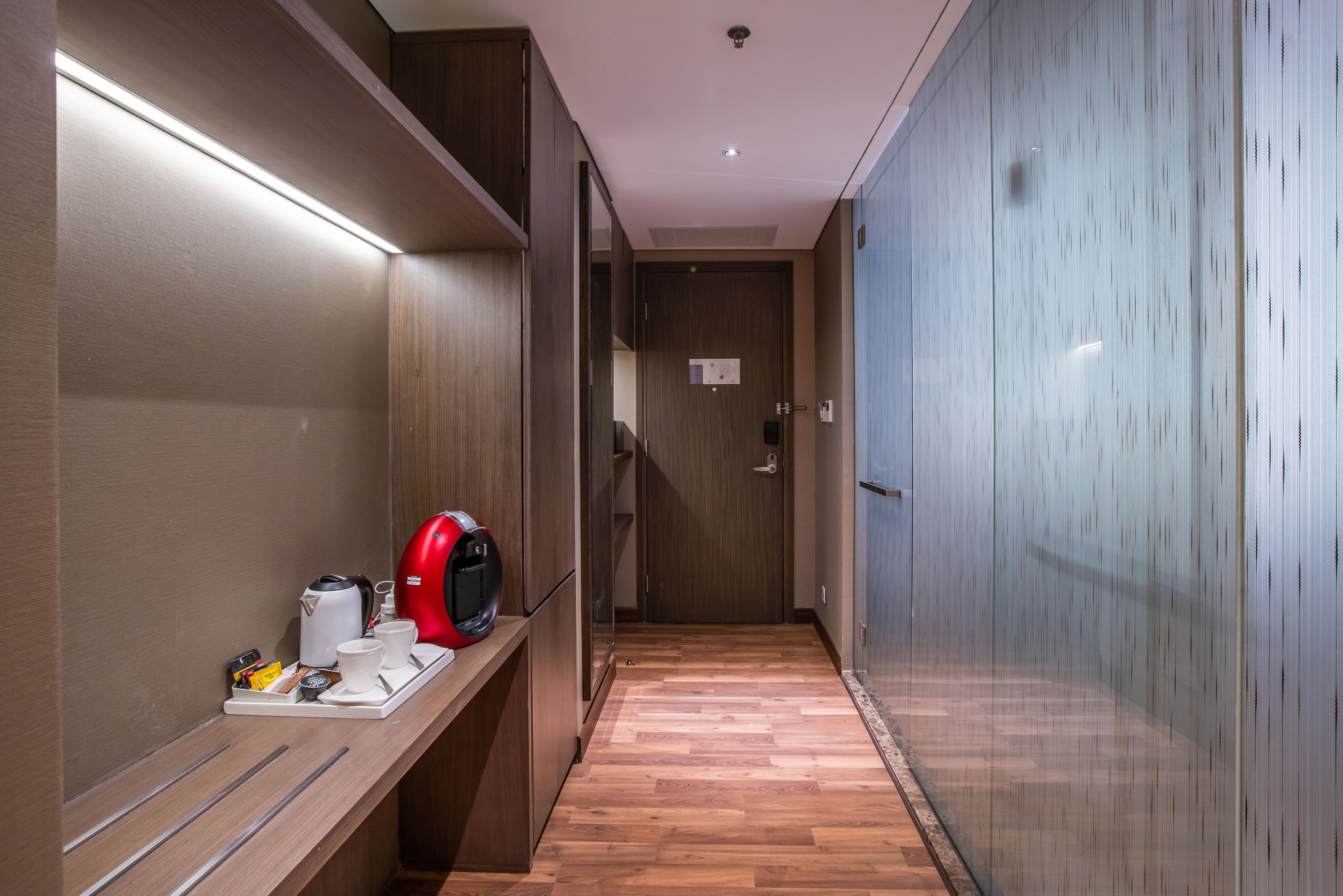 A hotel corridor with wooden flooring, a coffee station, and a door with a lock.