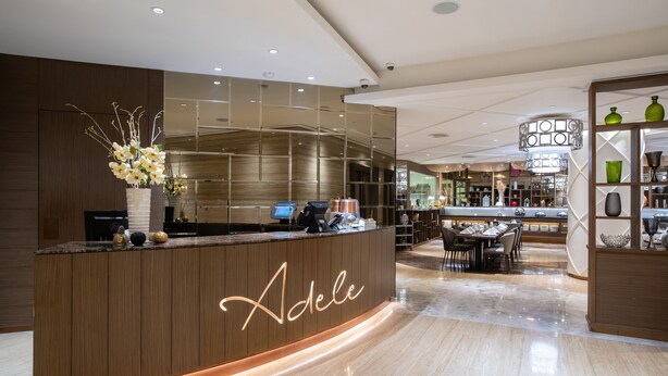 A modern hotel reception area with a wooden reception desk, a seating area with tables and chairs, and a bar in the background. - Ashley Wahid Hasyim Jakarta (Jakarta)