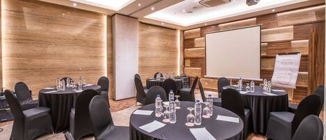 A conference room with round tables, black chairs, water bottles, and a presentation screen.