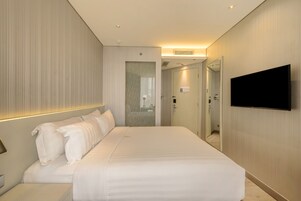 Una habitación de hotel moderna con una cama grande, un televisor de pantalla plana montado en la pared y un vestidor.