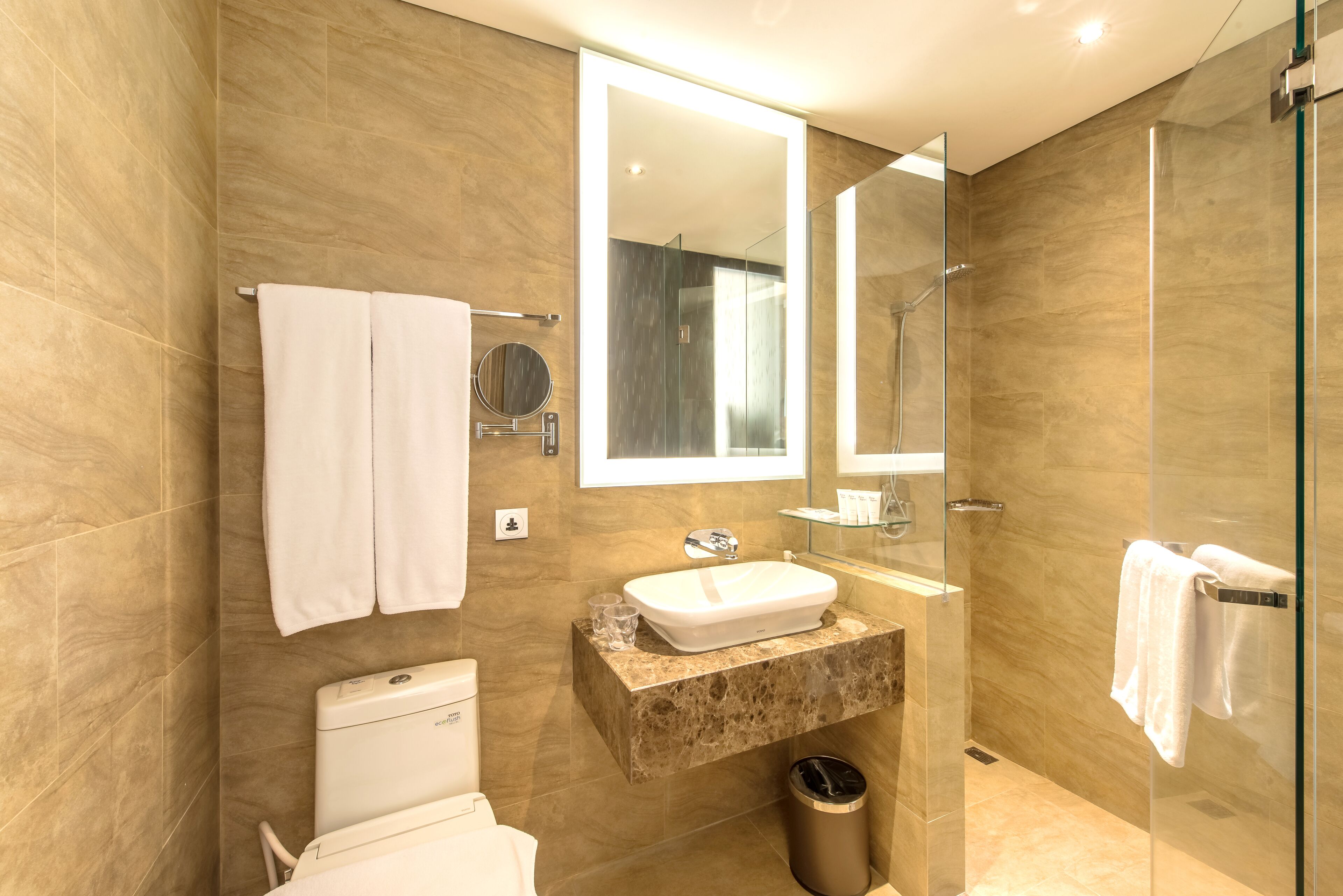 Un baño moderno con lavamanos de mármol, cabina de ducha con mampara de vidrio y un inodoro.