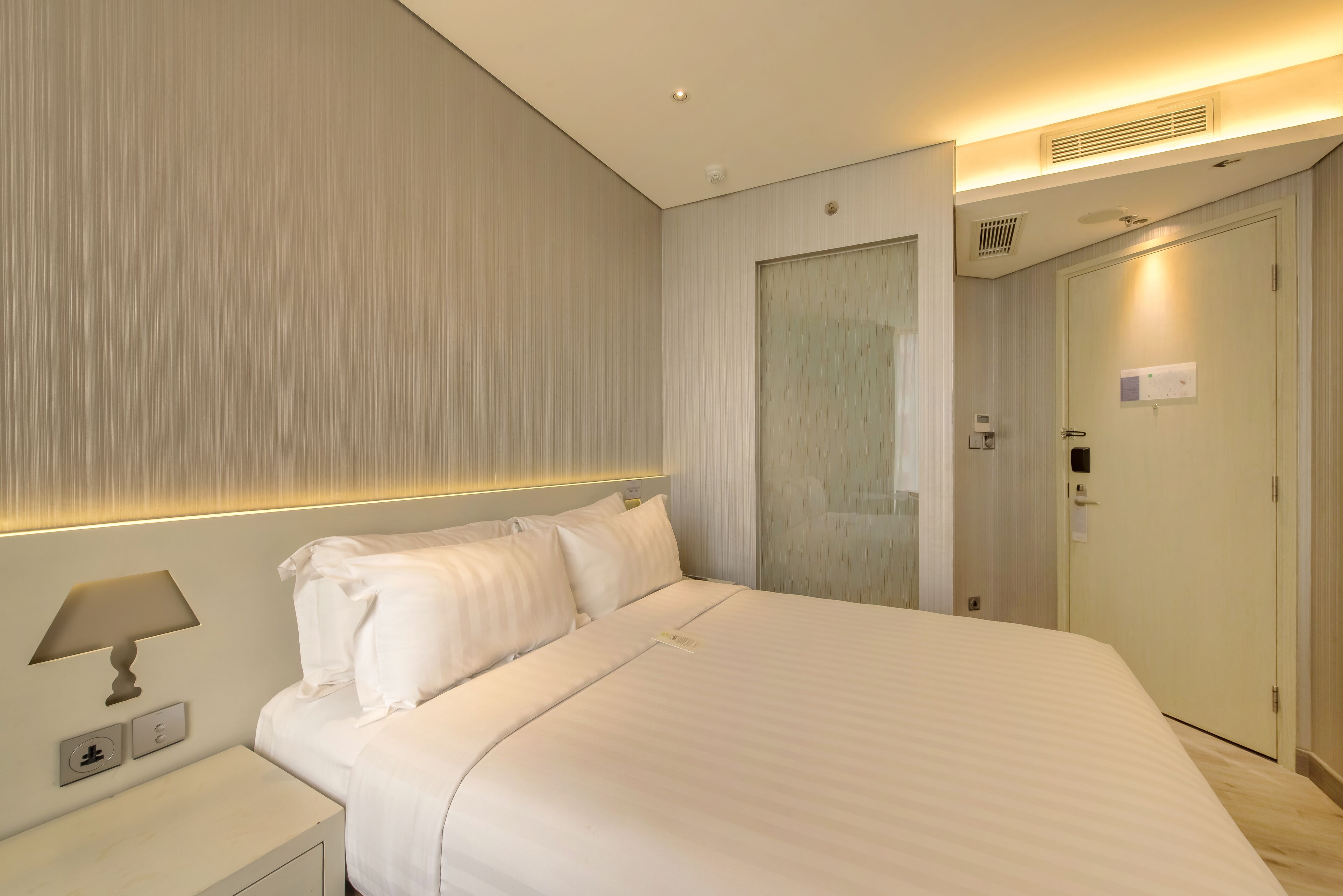 Una habitación de hotel con una cama grande, una mesita de noche con una lámpara y una puerta con un letrero.