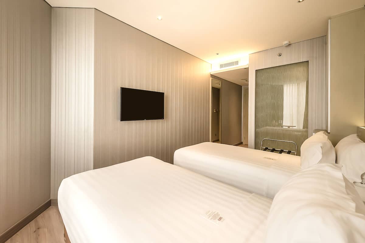 A hotel room with two beds, a flat-screen TV mounted on the wall, and a large mirror above the bed.