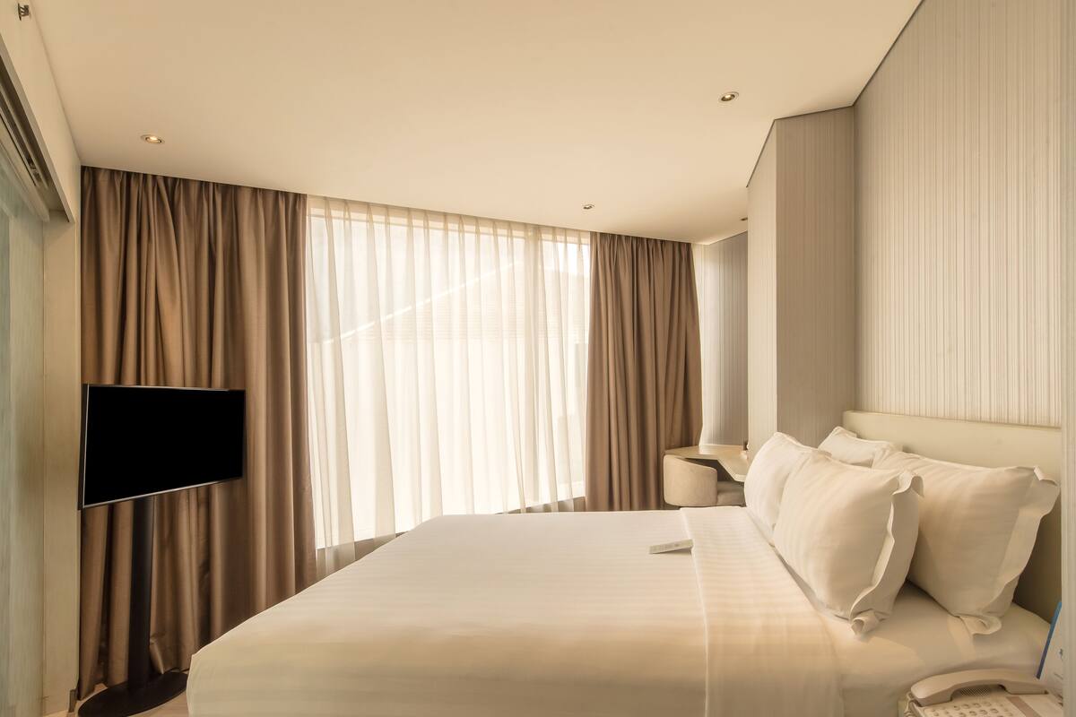 A hotel room with a large bed, a flat-screen TV mounted on the wall, a bedside table with a lamp, and a telephone.