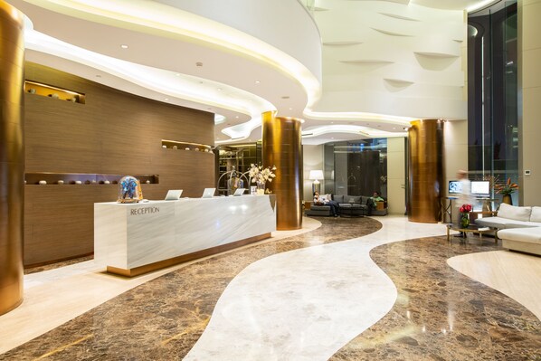 A modern reception area with a marble floor, a reception desk labeled "RECEPTION," and a seating area with a sofa and a coffee table. - Ashley Wahid Hasyim Jakarta (Jakarta)