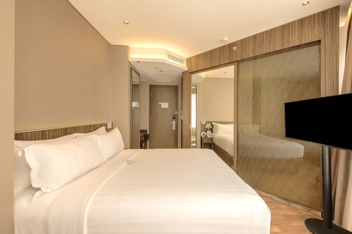 A hotel room with a large bed, a television, a mirror, and a wardrobe.