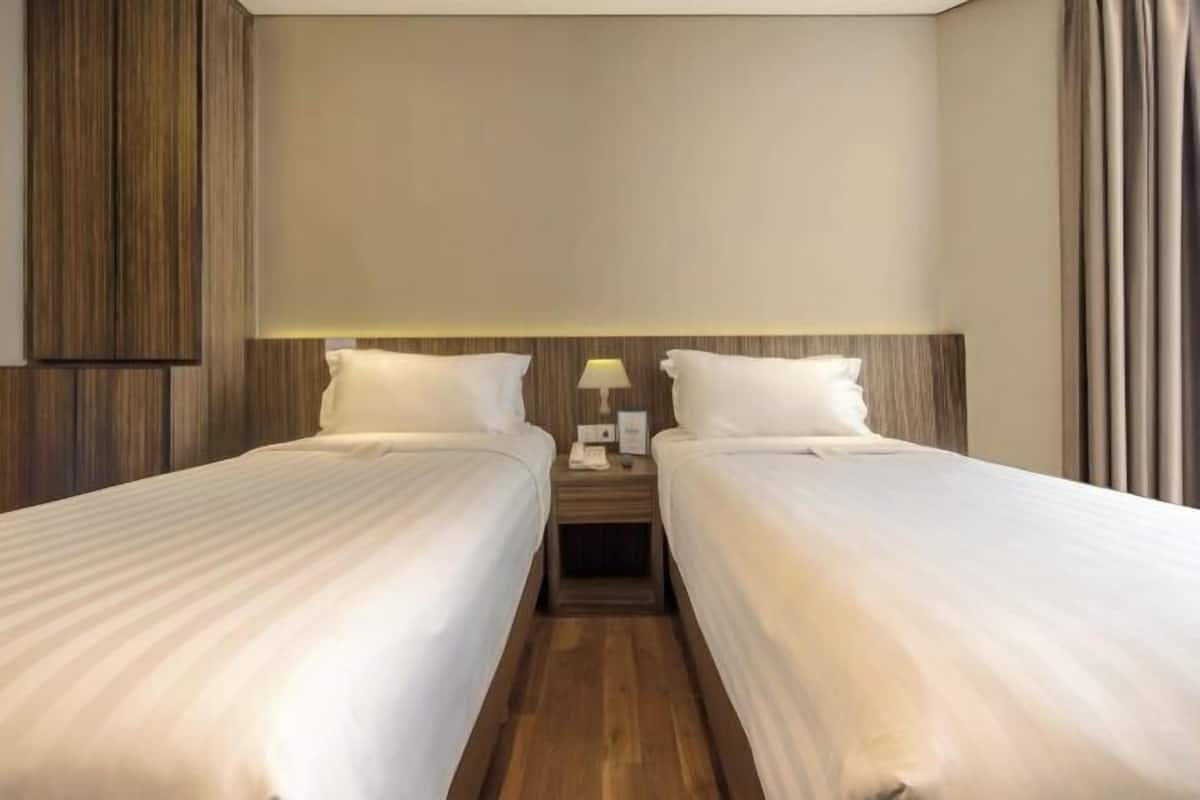 A hotel room with two single beds, a wooden headboard, a nightstand with a lamp, and a wall-mounted telephone.