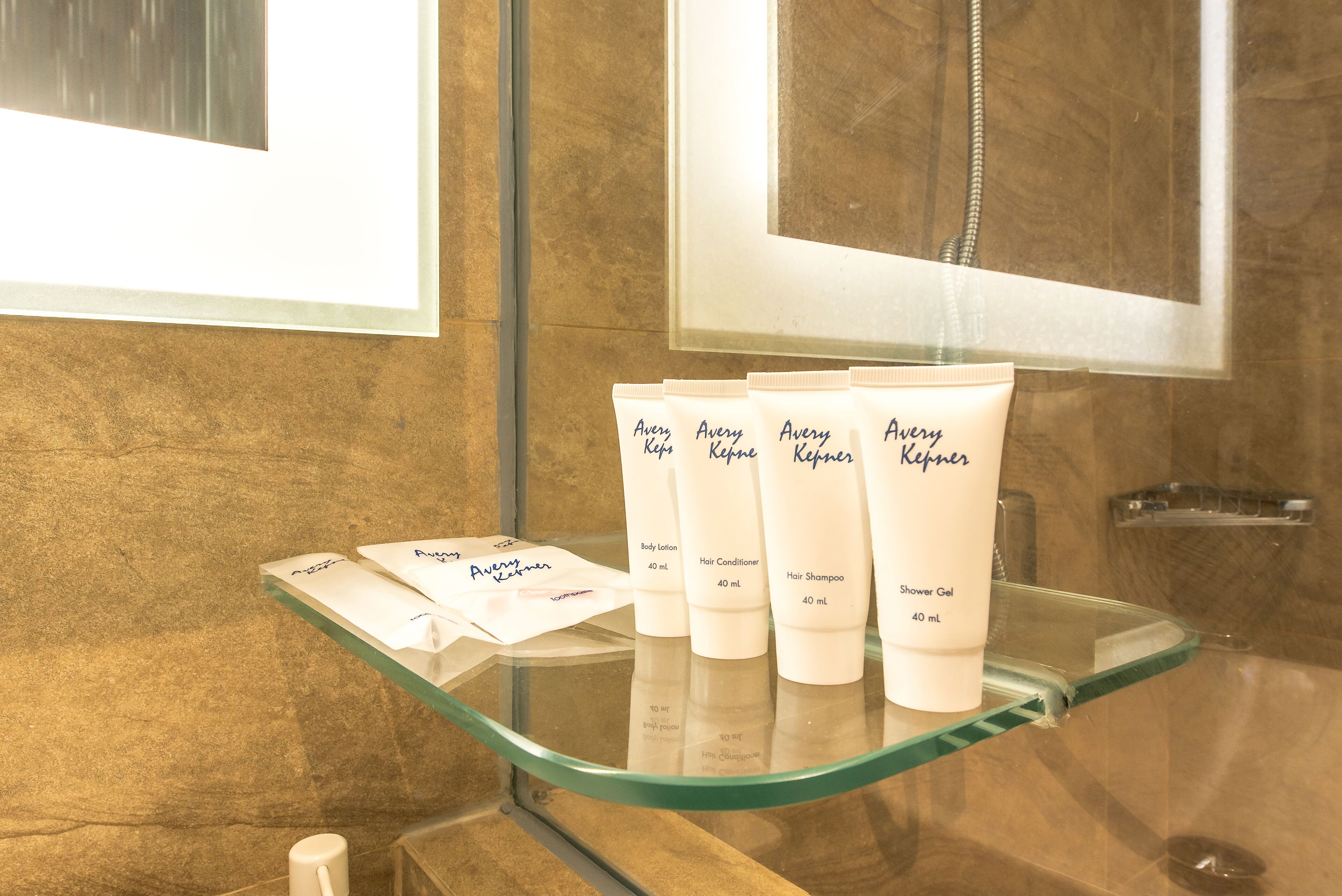 Un baño con un estante de vidrio que muestra diversos artículos de aseo, como loción corporal, acondicionador para cabello, champú y gel de ducha.