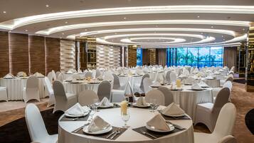 Un salón de banquetes con mesas redondas dispuestas para un evento formal, con manteles blancos, sillas y centros de mesa.
