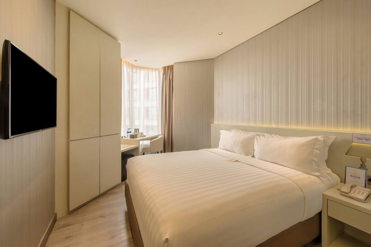 A hotel room with a large bed, a desk, a television, and a telephone.