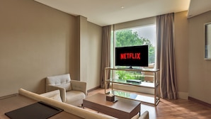 A modern living room with a sofa, a coffee table, and a TV mounted on a glass wall. - Ashley Wahid Hasyim Jakarta (Jakarta)