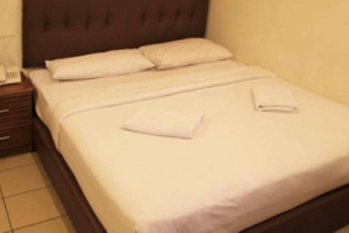 Een net opgemaakt bed met witte lakens en kussens, een houten hoofdbord en een nachtkastje met een telefoon.