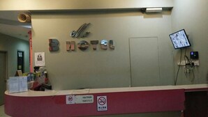 Un comptoir d’accueil d’hôtel avec une enseigne indiquant « Hôtel B » et un panneau « défense de fumer ».