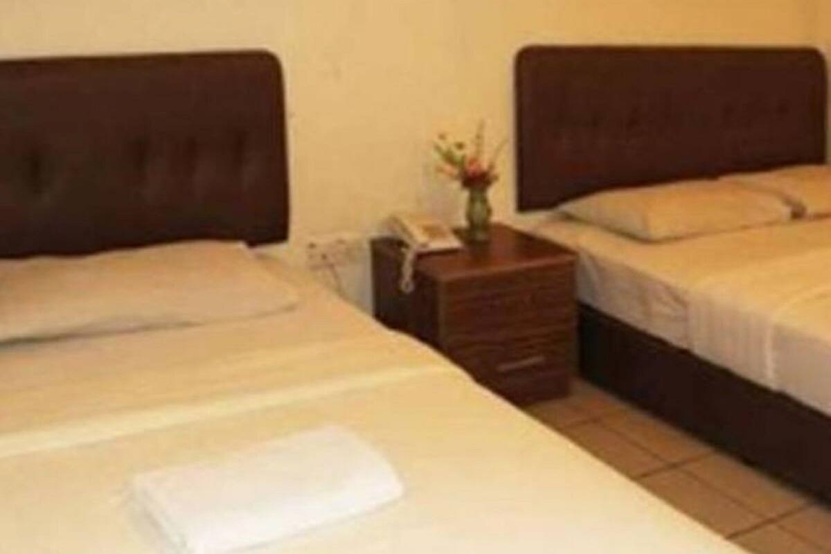 Een hotelkamer met twee eenpersoonsbedden, een klein nachtkastje met een vaas, en een effen muur.