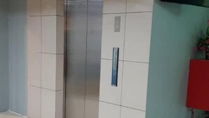 Un hall d’entrée propre et moderne, avec un sol carrelé, un grand ascenseur et un téléviseur à écran plat fixé au mur.