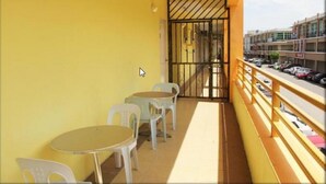 A balcony with two tables and chairs, a yellow wall, and a view of the street. - One Hotel Lintas Jaya (Kota Kinabalu)